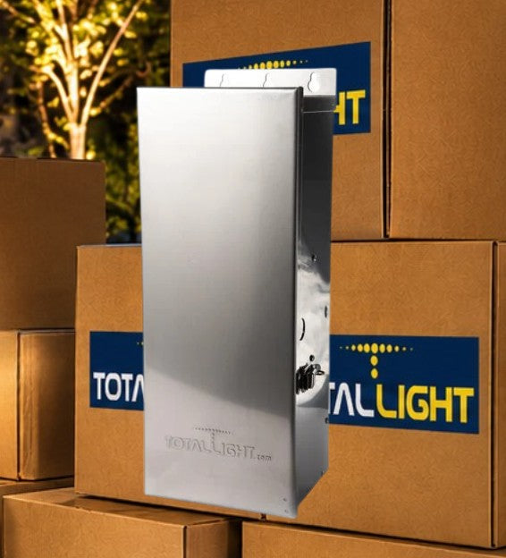 A tall, brushed-metal rectangular product stands in front of stacked brown cardboard boxes. The front box has a blue and yellow TotalLight logo sticker, and the product itself appears branded with 'ROYAL-LIGHT' near the bottom.