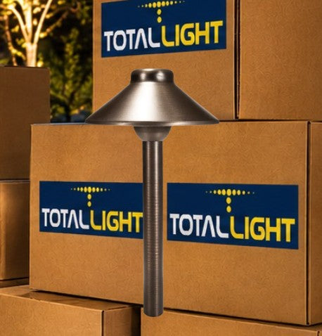 A TotalLight pathlight with a brushed metal dome shade and textured post, standing in front of stacked cardboard boxes with TotalLight branding.