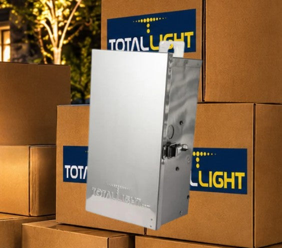 A silver metal outdoor light control box shown floating in front of stacked brown cardboard boxes with blue and yellow TotalLight logos.