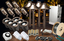 Load image into Gallery viewer, Outdoor lighting kit with multiple bronze-colored landscape lights, ground stakes, a spool of wire, wiring tools, a junction box, and a white control module, arranged against a dark nighttime patio background.
